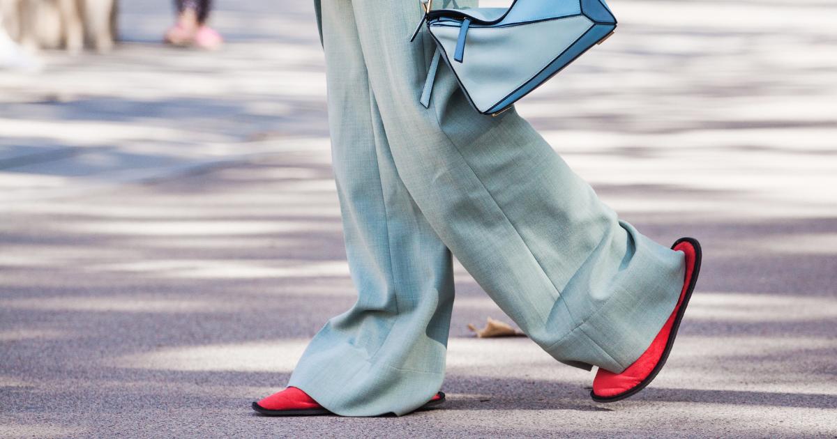 Close-up fashion trend featuring long light blue work pants paired with vibrant red slip-on shoes.