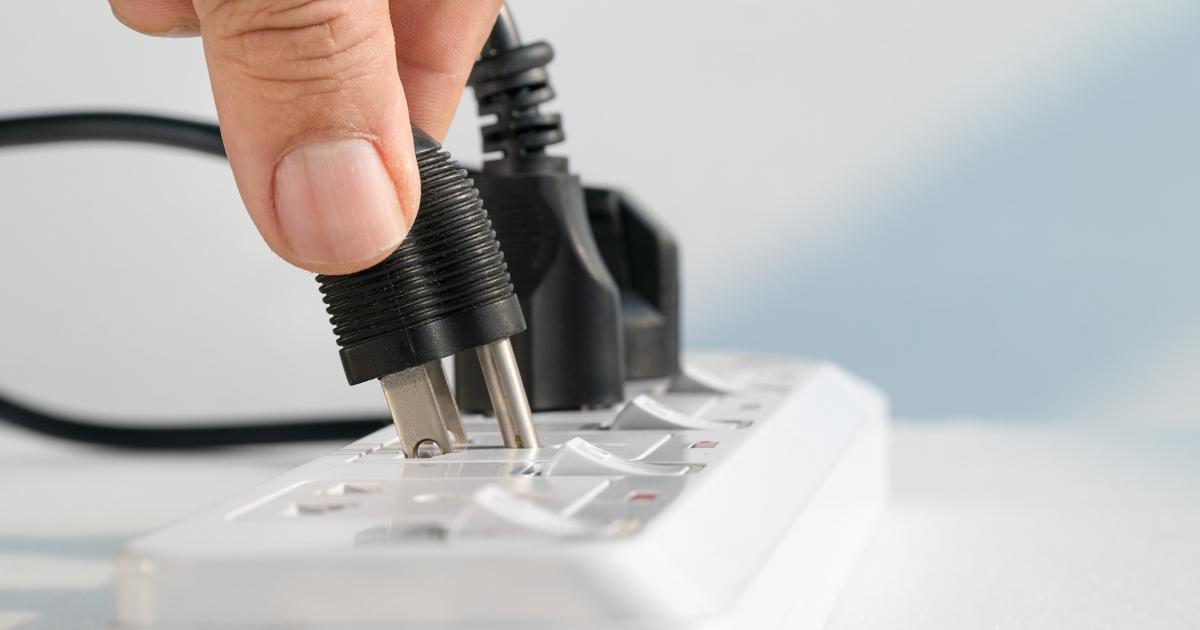 Close-up of a hand plugging a device into a powerboard reducing home energy.