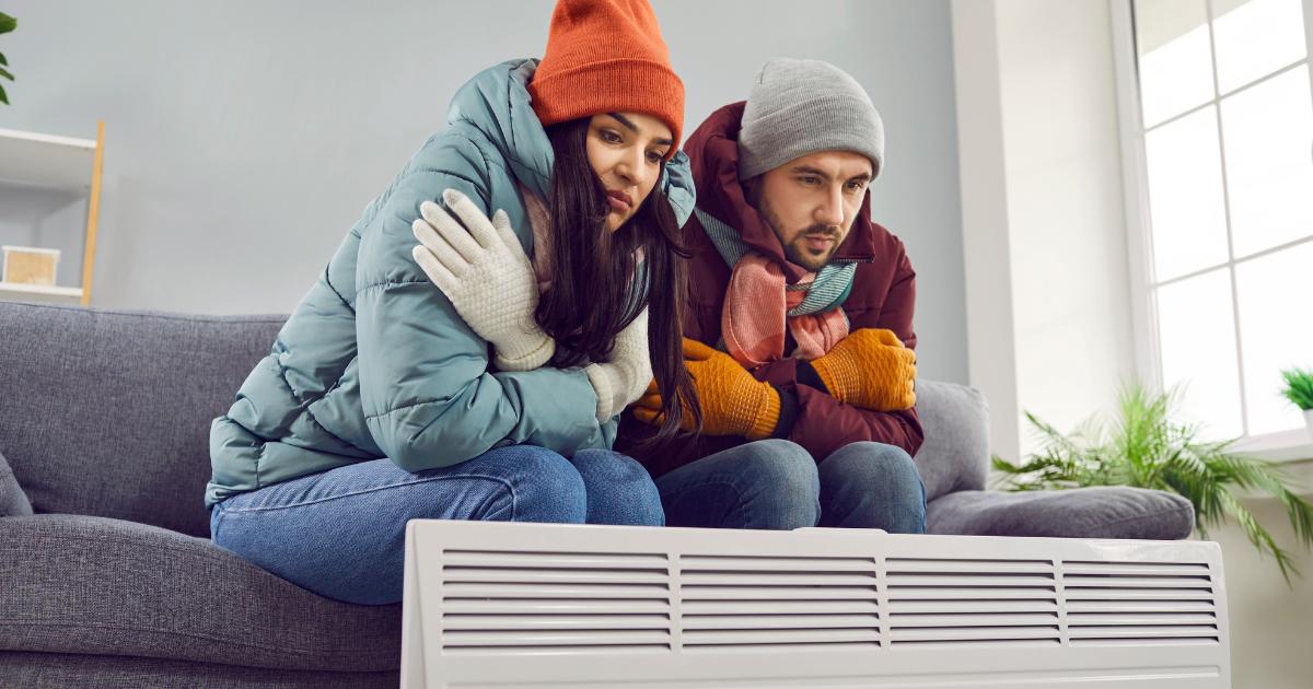 A couple shivering next to a heater, attempting to reduce their home energy usage and stay warm.