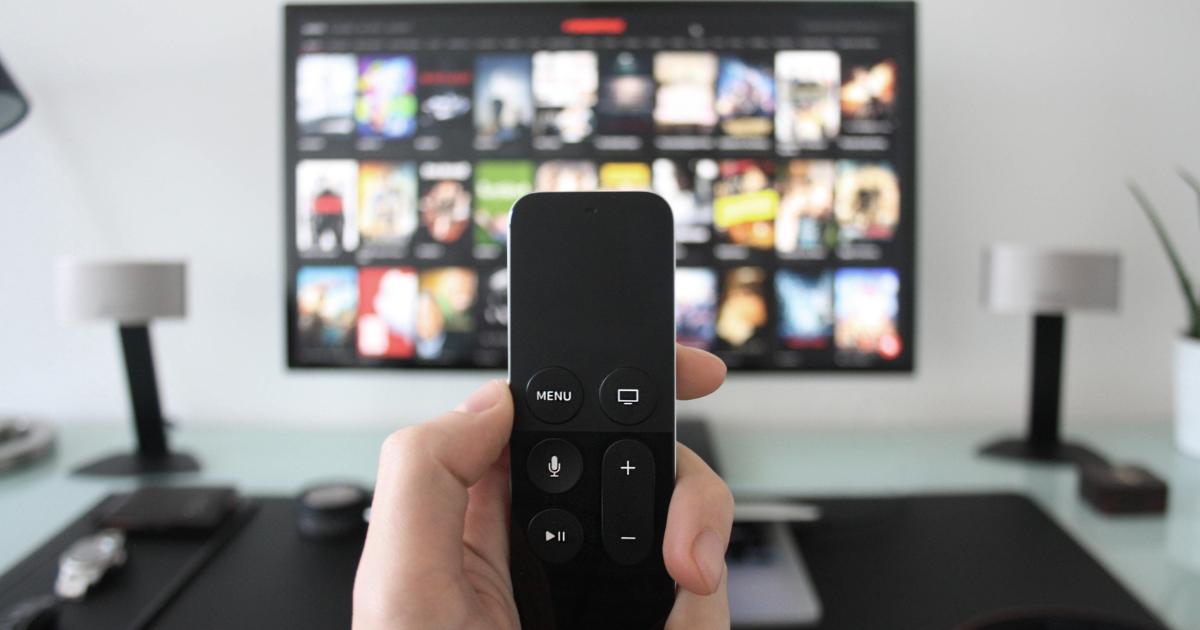 Close-up image of a hand holding and controlling a TV remote, highlighting the buttons and display.