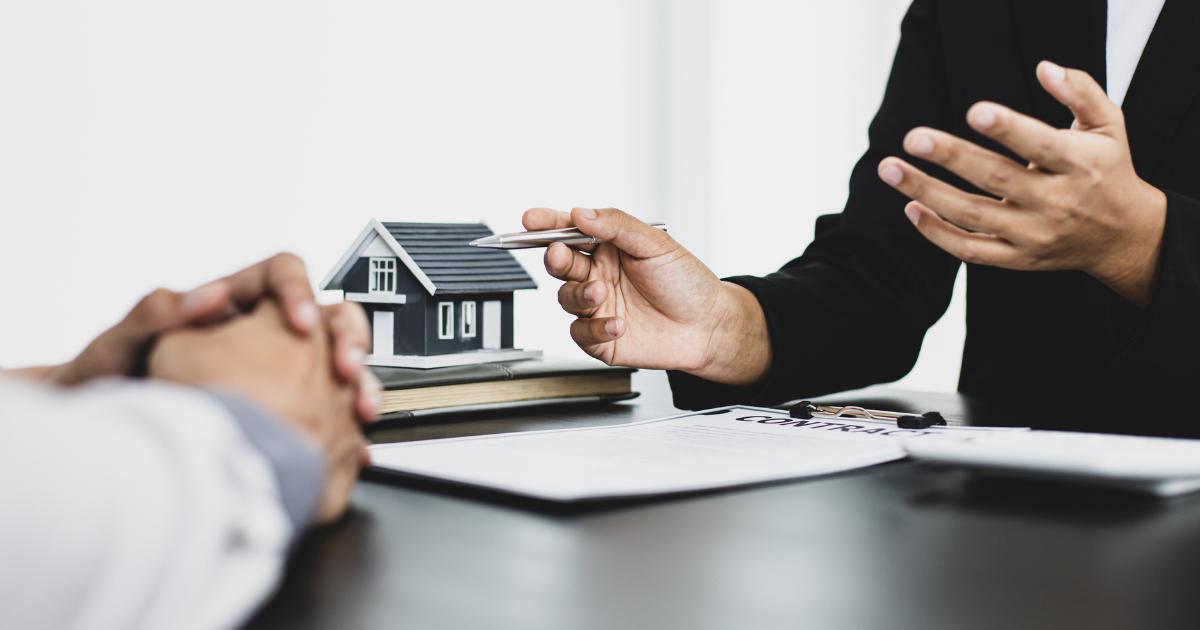 Close-up of two people's hands discussing buying a home, with documents and notes in view.