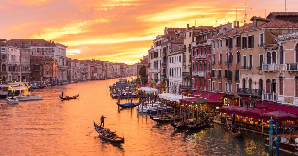 A stunning sunset over Venice, Italy, with gondolas drifting along the canals and vibrant skies casting a warm glow over historic buildings, perfect for Instagram travel.