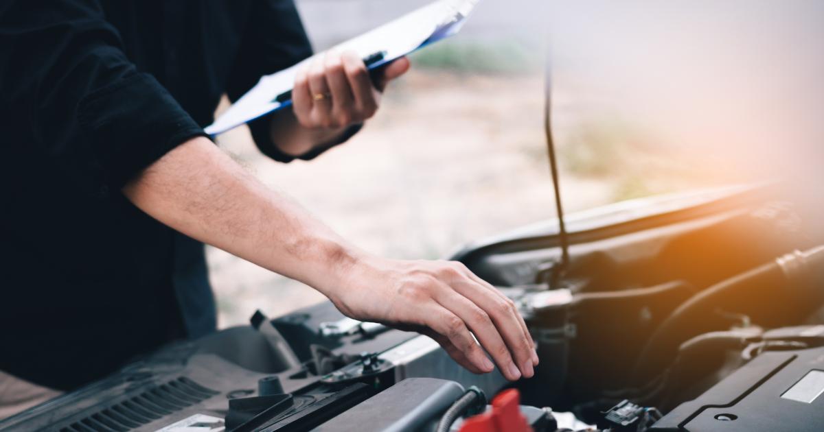 Close-up of a man's hand near the battery terminal during a car inspection.