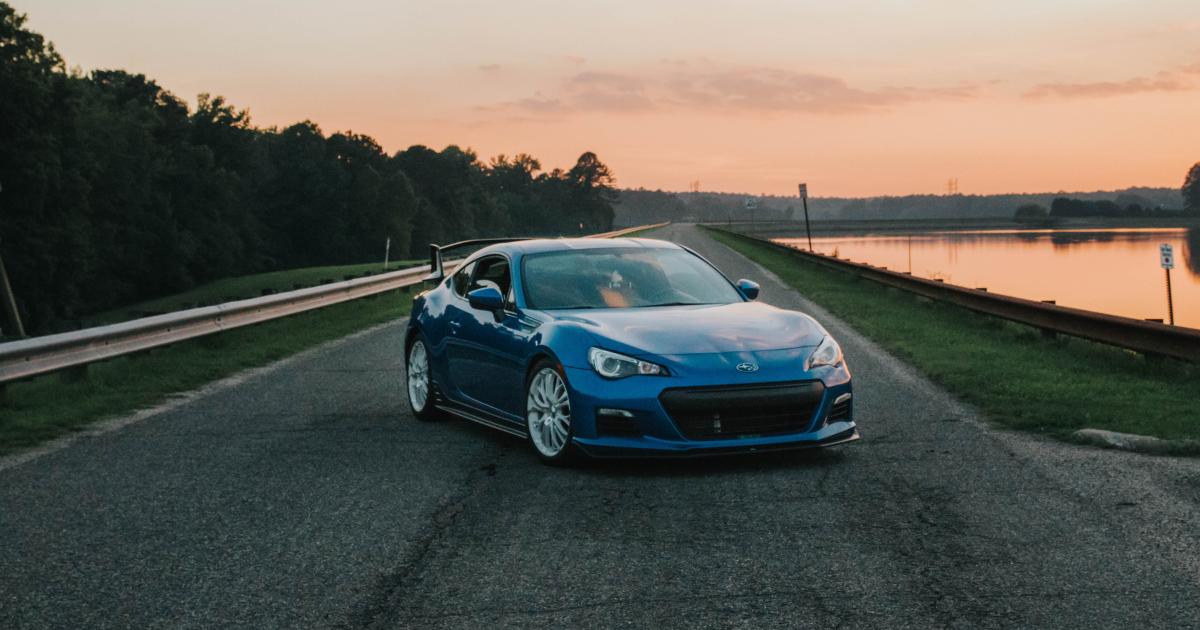 A Subaru BRZ new car parked on a serene, long road beside a tranquil lake, showcasing its sporty design against a peaceful backdrop.