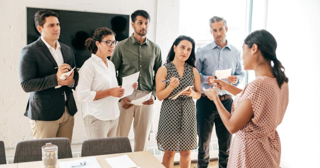 A diverse work team gathered in a modern office for a stand-up meeting, engaging in leadership programs and collaboration.