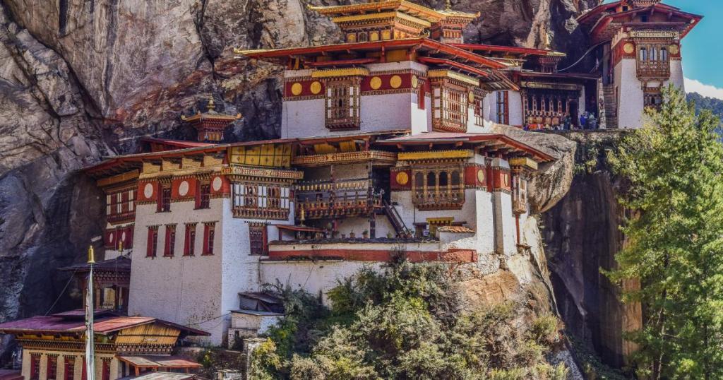 A serene view of hidden gems in Bhutan, showcasing a picturesque hillside village surrounded by lush green mountains and misty clouds.